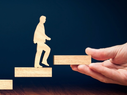 Wooden figure being given wooden stairs to climb by a person off screen