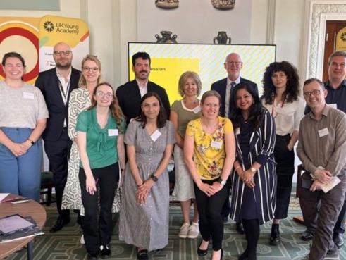 A group of UK Young Academy Members and workshop leaders pose smiling for a group photo in the British Academy