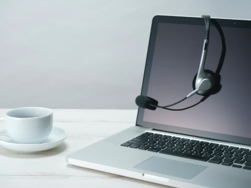 Laptop with headphones with a microphone looped over. A cup of a hot drink is on the side of the laptop.