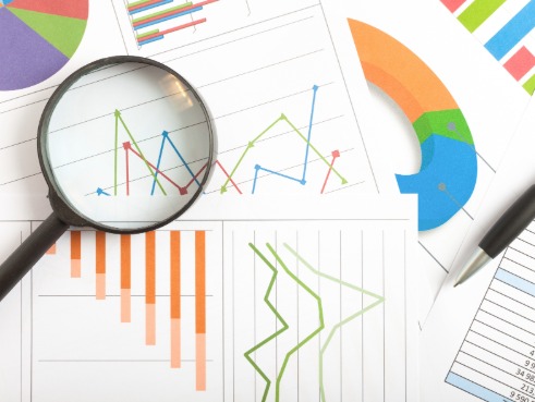 A magnifying glass sits on top of different bits of paper with graphs and statistics on them.
