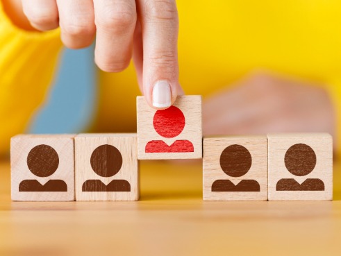 Lineup of wooden blocks with people on them. One is being picked out and is highlighted from the rest
