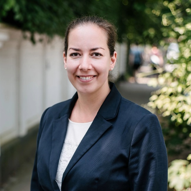 Woman smiles at the camera outside in a blue suit jacket