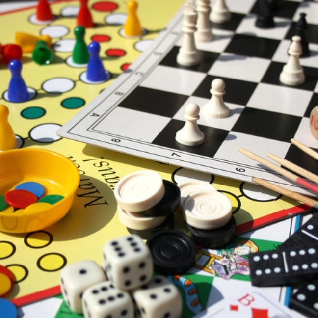 An array of board games, including chess, a series of die, counters and cards scattered