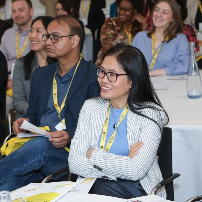 Members sit watching a presentation, engaged and smiling