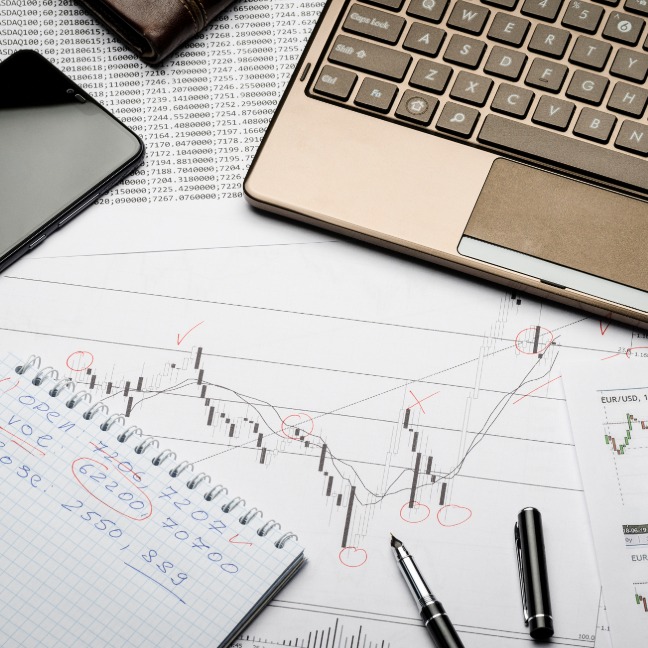 A messy desk with a laptop, phone, pens, a notepad, and graphs scattered