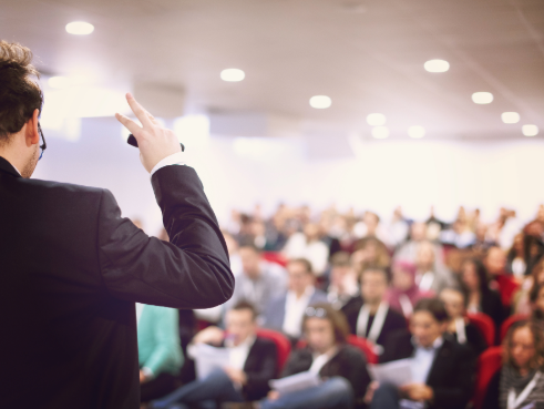 Man stands in front of a crowd to present, as they read a report.