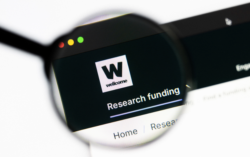 Wellcome website page about research funding viewed through a magnifying glass on a computer screen.